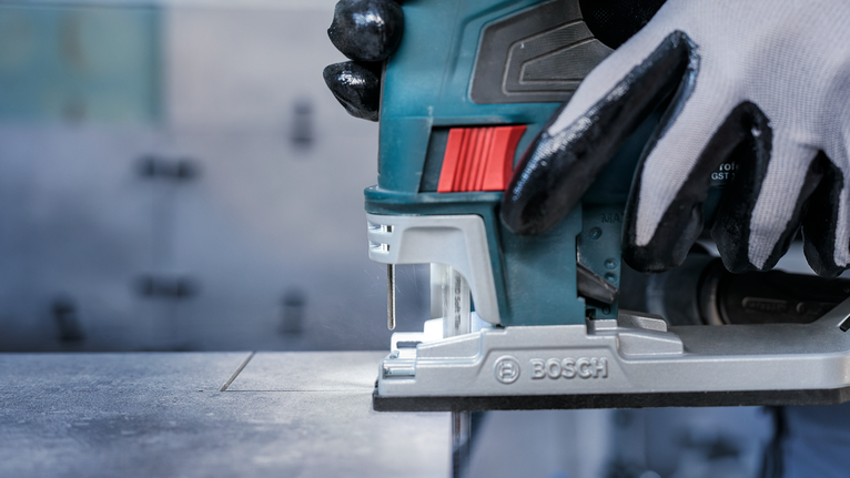 佩戴安全设备的人员使用曲线锯在金属板上切割出一条直线。