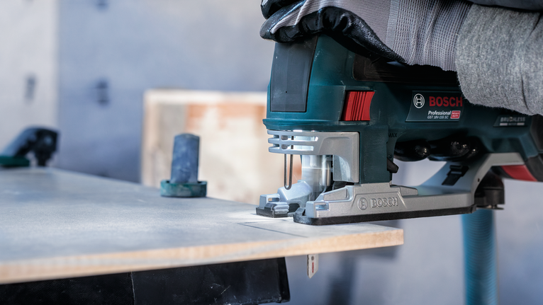 佩戴安全设备的人员使用电动曲线锯切割木材。