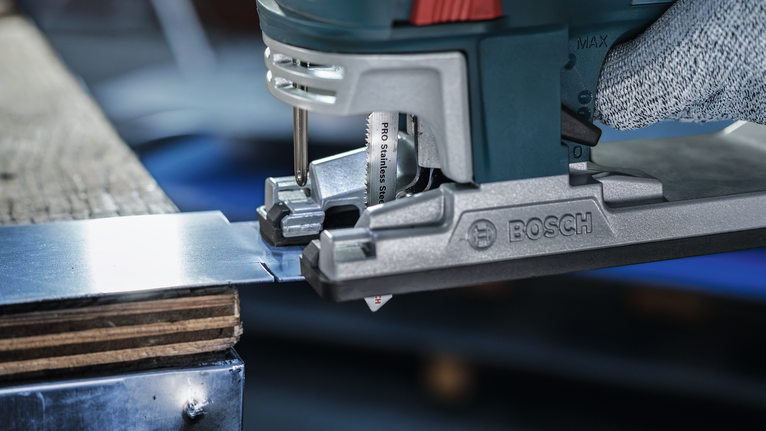 佩戴安全设备的人员用曲线锯切割金属板。