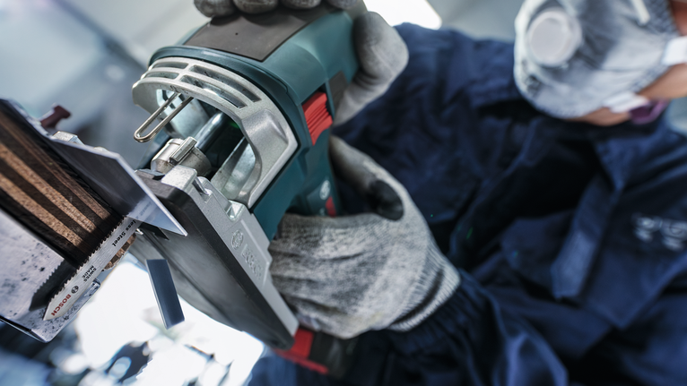 一名佩戴安全设备的人员操作电动工具切割金属片。