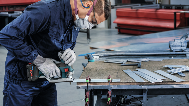 一名佩戴安全设备的人员在工作台上用电锯切割金属板。