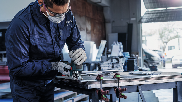 佩戴安全设备的人员使用电动工具在工作台上打磨金属。