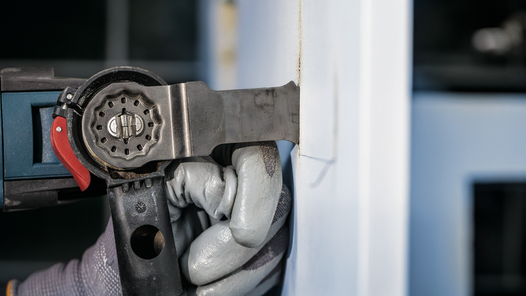 佩戴安全设备的人员使用电动工具切割墙壁。