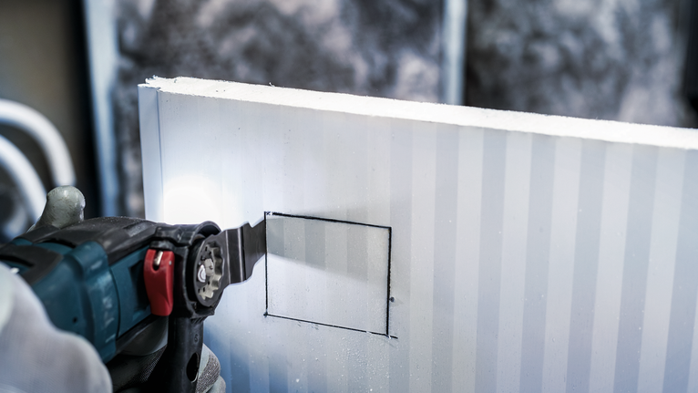 佩戴安全设备的人员使用电动工具在干墙上切割方形开口。