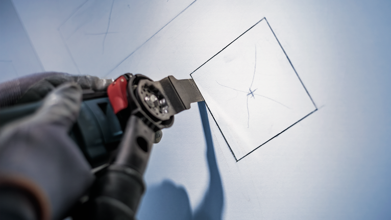 佩戴安全设备的人员使用电动工具在干墙上切割出一个正方形。