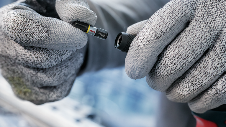 佩戴安全设备的人员将螺丝刀头放在钻头附件附近。