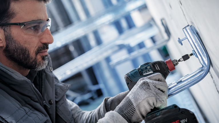 佩戴安全设备的人员使用无绳电钻安装金属支架。