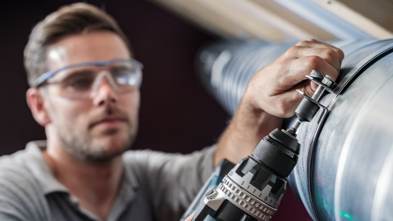 佩戴安全设备的人员使用电钻将螺栓紧固到金属管道上。