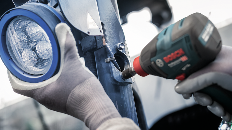 佩戴安全设备的人员使用电动工具将金属支架固定在灯附近。