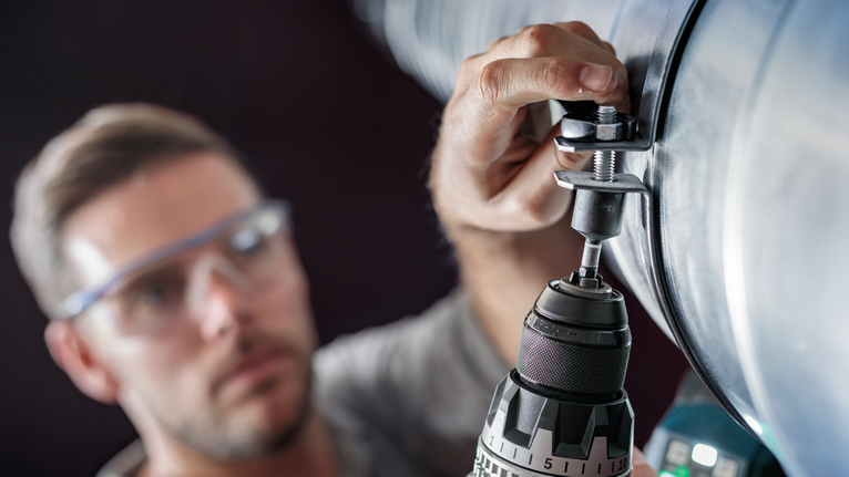 穿着安全设备的人员在一根大金属管上钻孔。