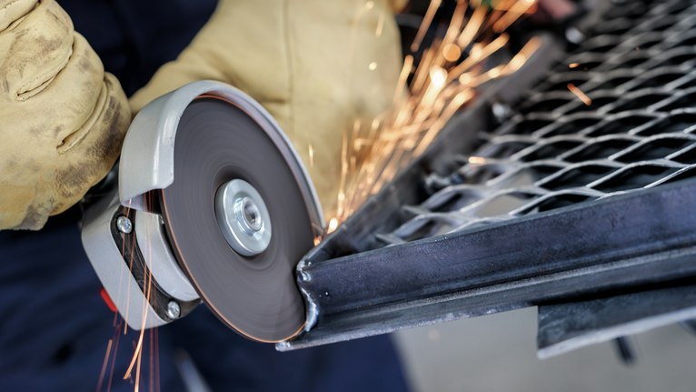 佩戴安全设备的人员使用旋转角磨机切割金属网。