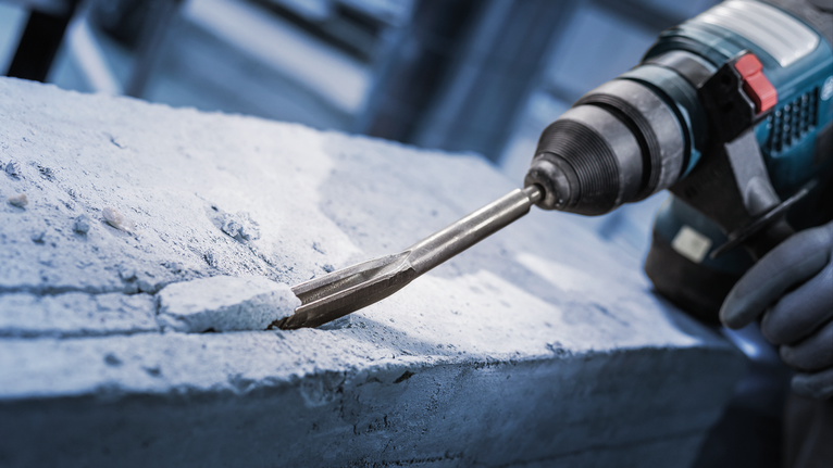 佩戴安全设备的人员用旋转锤凿混凝土。