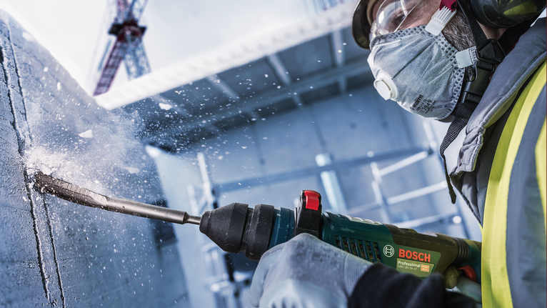 一名佩戴安全设备的人员在混凝土中钻孔，产生飞溅的碎片。