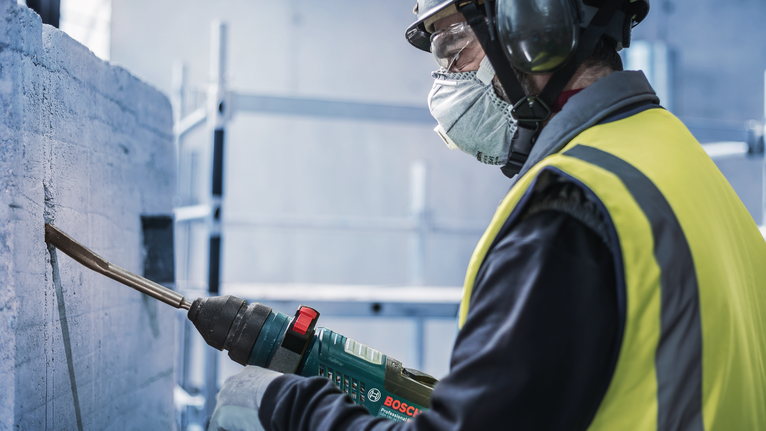 佩戴安全设备的人员使用电动工具凿混凝土。