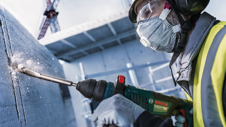 穿着安全设备的人员在建筑工地上钻入混凝土。