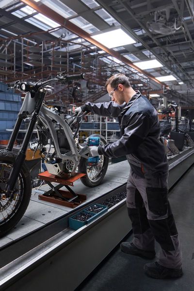 一名佩戴安全装备的人员使用冲击起子组装摩托车车架。.