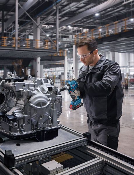 一名佩戴安全设备的人员使用无绳冲击扳手修理发动机组件。.