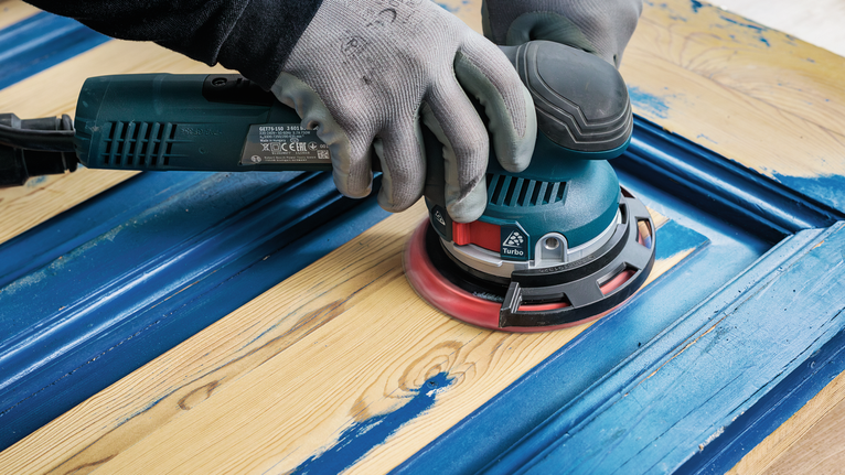 一名佩戴安全设备的人员正在打磨木门上的蓝色油漆。