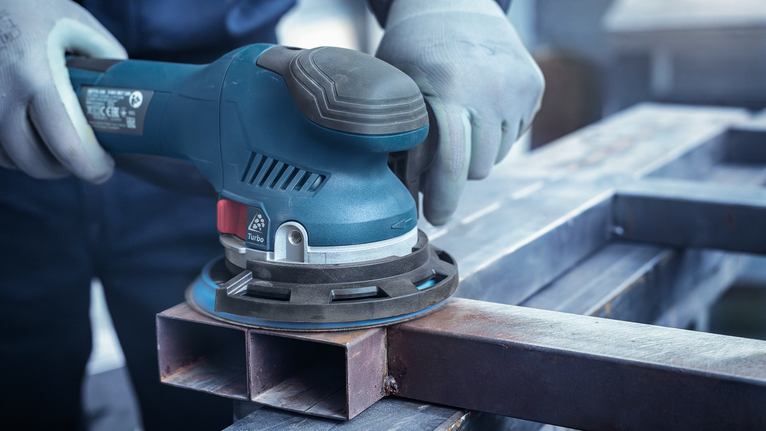 一名佩戴安全设备的人员正在使用电动砂光机打磨金属表面。