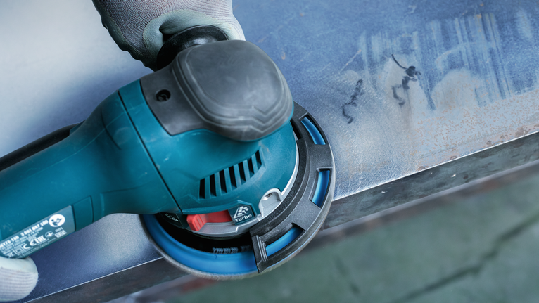 佩戴安全设备的人员使用电动工具打磨金属表面。