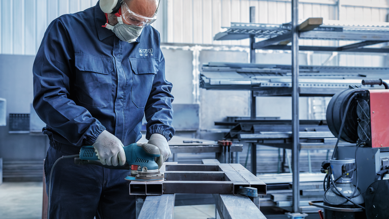 一名佩戴安全设备的人员在工业车间内打磨金属梁。