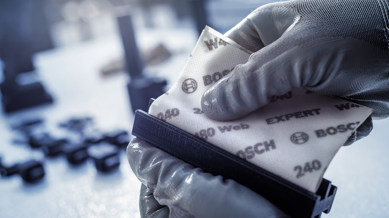 佩戴安全设备的人员将砂纸固定在砂磨块上。