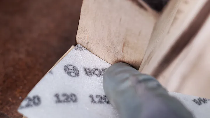 穿着安全设备的人正在打磨木质表面的角落。