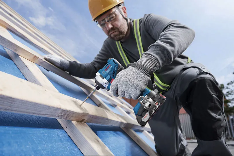 一名佩戴安全设备的人员使用无绳电钻将螺丝拧入木梁。.