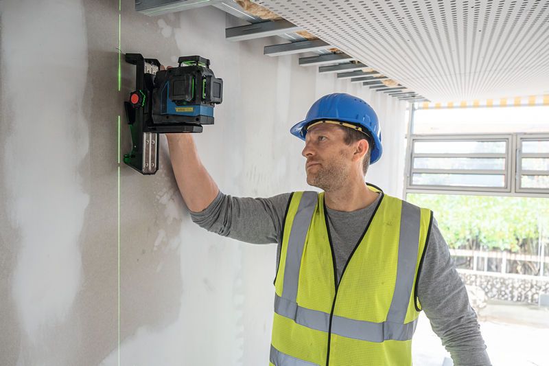 一名佩戴安全设备的人将激光调平工具对准墙壁。.