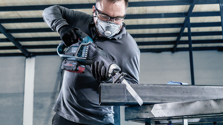 一名佩戴安全设备的人员使用往复锯切割金属梁。