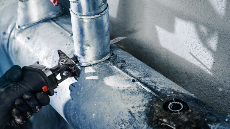 佩戴安全设备的人员用往复锯切割金属管。