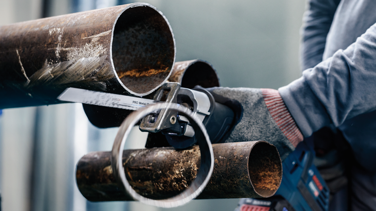 佩戴安全设备的人员用往复锯切割金属管。