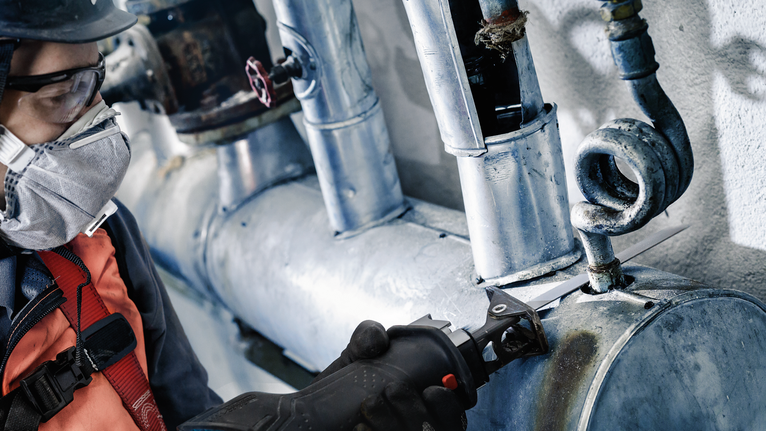 一名佩戴安全设备的人员用往复锯切割金属管。