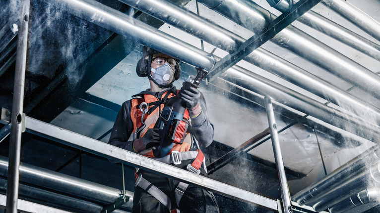 穿着安全设备的人员正在钻入脚手架上的金属管道。