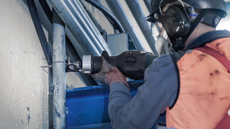 佩戴安全设备的人员用往复锯切割金属管。