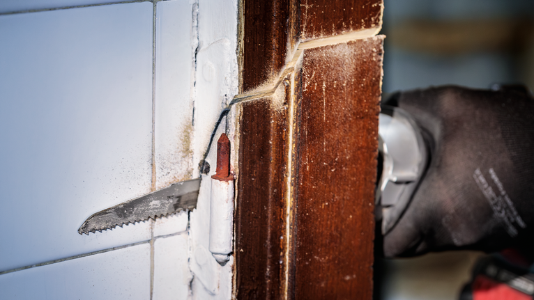 一名佩戴安全设备的人员使用电动工具切割木门框。