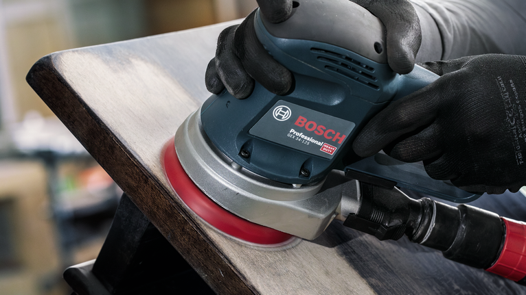 佩戴安全设备的人员使用电动砂光机打磨木质表面。