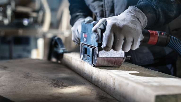 一名佩戴安全设备的人员正在使用电动工具打磨木梁。