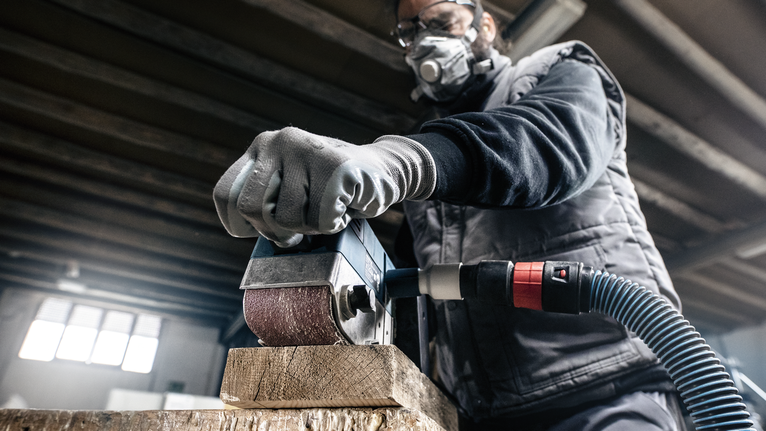 一名佩戴安全设备的人员正在用电动砂光机打磨木梁。
