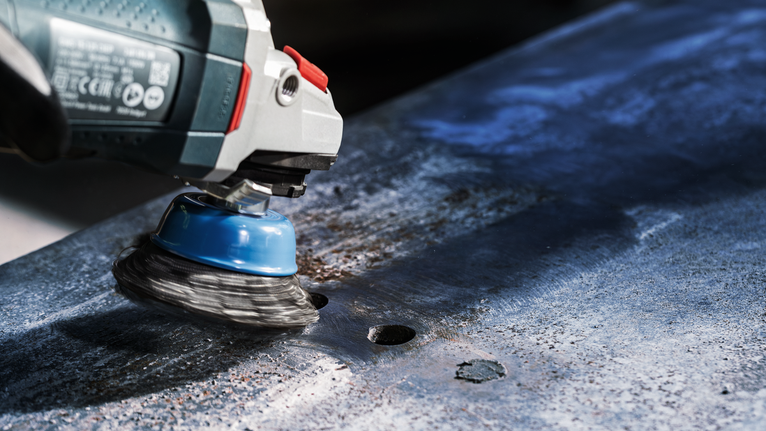 带有钢丝杯刷的电动工具可以磨掉金属板上的铁锈。