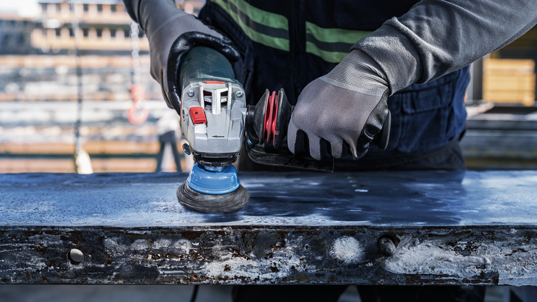 佩戴安全设备的人员使用电动工具打磨金属表面。