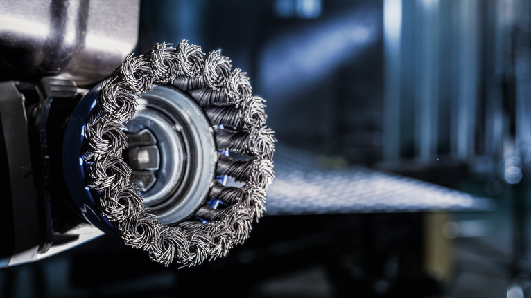 附在电动工具上的用于金属表面处理的金属丝杯刷的特写。