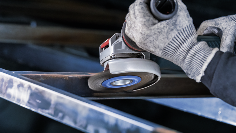 佩戴安全设备的人员使用角磨机打磨金属梁。