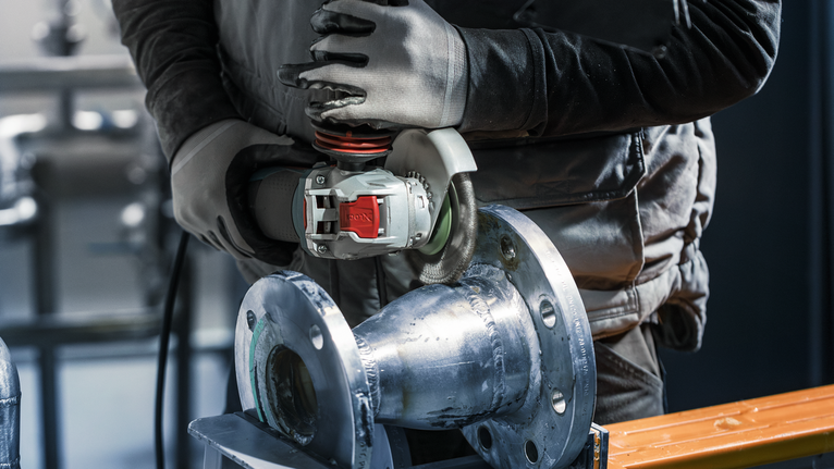 佩戴安全设备的人员使用角磨机打磨金属管。