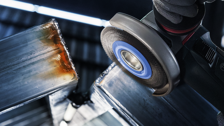 佩戴安全设备的人员使用角磨机打磨金属梁的边缘。