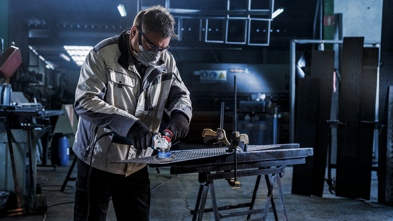 工厂里，穿着安全设备的工人在工作台上打磨金属。