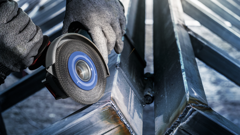 佩戴安全设备的人员使用电动工具研磨金属梁。