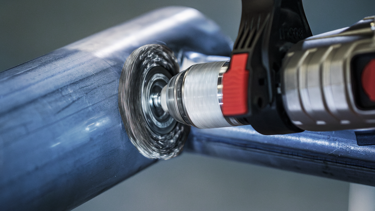 带有钢丝刷附件的电钻正在抛光金属管。