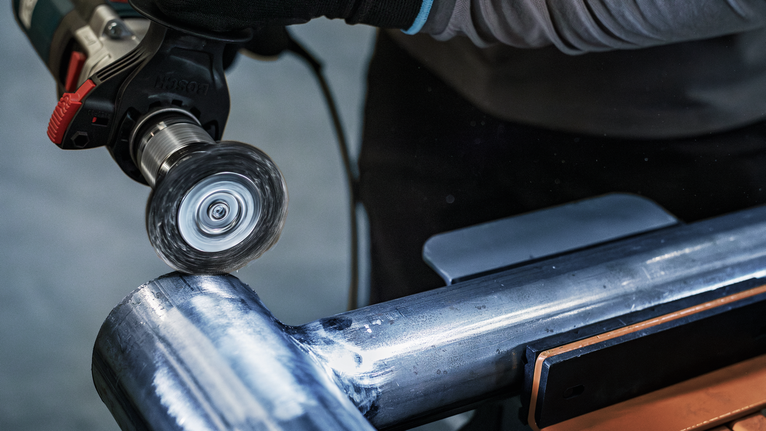 佩戴安全设备的人员使用旋转工具抛光金属管道。