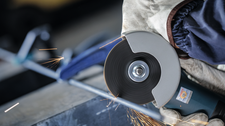 佩戴安全设备的人用角磨机切割金属，火花四溅。